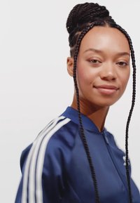 Navy blue track jacket with white stripes on sleeves, zip closure, smooth texture. Braided hair styled in a bun, neutral background.