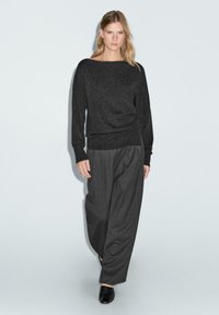 Dunkelgrauer Strickpullover mit weitem Ausschnitt, kombiniert mit locker sitzenden dunkelgrauen Hosen, getragen mit schwarzen Slippern. Schmeichelnde Textur.