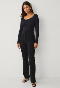 Zwart langemouwen top gecombineerd met hoge zwarte broeken, met een aansluitend ontwerp en een gladde textuur. Compleet met open teen zwarte hakken.