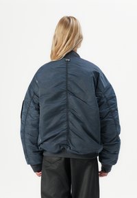 Polstret bomberjakke i dyp marineblå, med ribbestrikket krage, elastiske mansjetter og en slank finish. Inkluderer en logotagg bak.