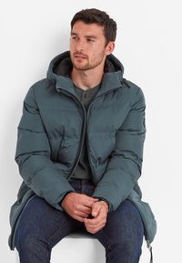Teal puffer jacket with a hood, featuring a zip closure, quilted texture, and elastic cuffs. Paired with a gray textured shirt and dark jeans.