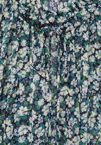 Blouse fleurie en tissu léger et transparent avec des fleurs bleues, vertes et blanches sur un fond sombre, dotée d'un design plissé et d'un col noué.