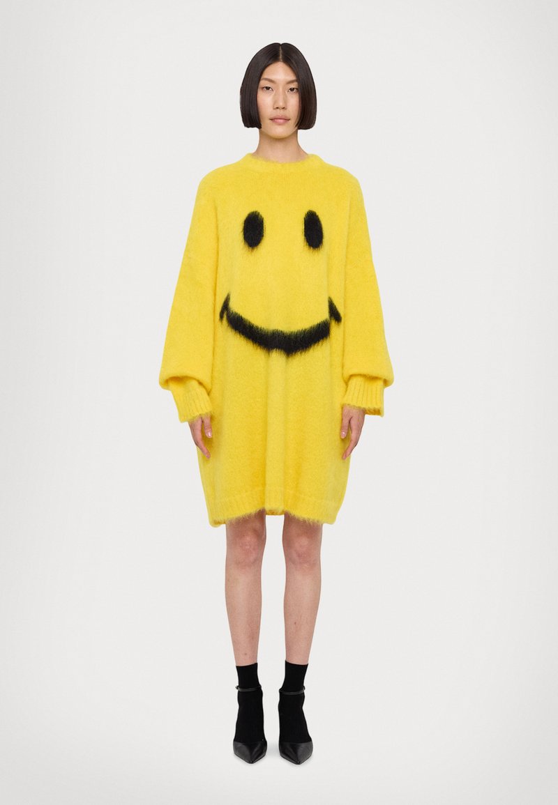 Abito in maglia oversize giallo realizzato in materiale morbido, caratterizzato da un design con faccina sorridente nera, polsini a costine e una vestibilità ampia.