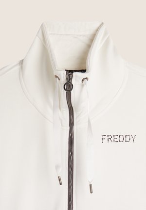 Veste blanche zippée avec col haut, dotée d'une fermeture éclair grise, de cordons de serrage et de "FREDDY" orné de strass sur le côté gauche.