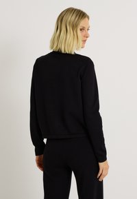 Pull en tricot noir à manches longues, col rond et design légèrement court. Texture lisse et silhouette simple sans motifs visibles.