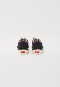 Zapatillas moradas y negras con parte superior de textil, suela de goma blanca y etiqueta de logo roja en el talón. Punta redondeada y diseño de corte bajo.