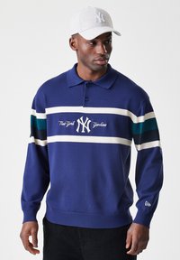 Mornarsko modra pletena polo majica z belimi in teal črtami, s svetlobreznim izvezenim logotipom "New York Yankees". Ujemajoča se lahka siva kapa.
