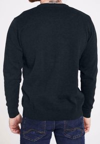 Maglione lavorato a maglia di un blu navy scuro con maniche lunghe, polsini e orlo a coste, indossato sopra dei jeans blu, mostrando una superficie liscia e un design semplice.