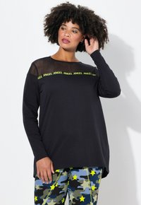 Zwarte lange mouwtop met netwerknauw en neon groene "ANGEL" opdruk, gecombineerd met gestreepte panty’s met sterren in blauwe en groene tinten.