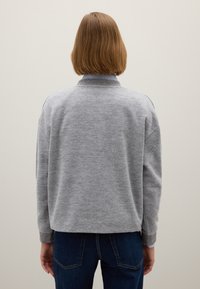 Grijze gebreide trui met een ronde hals, lange mouwen en geribbelde manchetten. Draagt over een blauwe gestreepte overhemd met kraag.