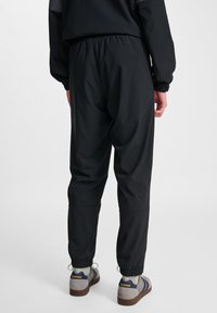 Svarta lätta joggers med elastisk midja, smalnade muddar och en mjuk yta, tillsammans med sneakers i retrostil.