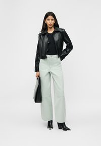 Γυναίκα που φοράει μαύρο κοντό δερμάτινο μπουφάν, μαύρο πουκάμισο, ανοιχτόχρωμο παντελόνι με φαρδιά πόδια, μαύρες μπότες με τακούνι, κρατώντας μια μαύρη τσάντα tote.