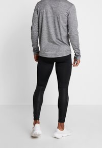 Maglietta grigia a maniche lunghe realizzata in un tessuto testurizzato, abbinata a leggings neri aderenti e scarpe da ginnastica bianche.