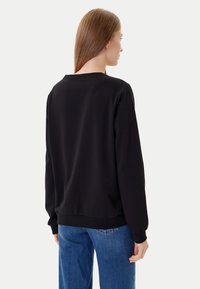 Felpa nera con vestibilità comoda, polsini a coste e un semplice scollo rotondo, abbinata a jeans di denim blu.