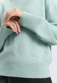 Jasnoniebieski dzianinowy sweter z żeberkowanymi mankietami i krawędzią, o miękkiej fakturze i luźnym kroju, podkreślający subtelne różnice kolorystyczne.