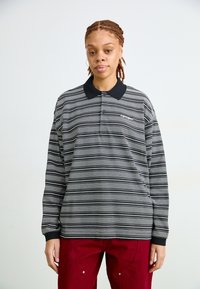 Polo a maniche lunghe a righe bianche e nere con colletto nero e logo sul petto. Caratterizzato da una vestibilità rilassata e polsini a coste.