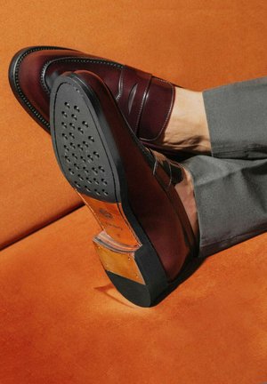 Burgunderfarbene Lederlofer mit glänzender Oberfläche, detaillierter Nahtführung und schwarzer Gummisohle mit kreisförmigen Traktionsmustern.