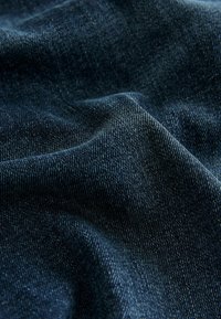 Dark blue denim fabric with a smooth, slightly textured surface, showcasing fine weave and subtle variations in color.