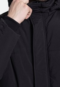 Schwarze Steppjacke mit hohem Kragen, glattem Stoff und elastischen Bündchen. Das Design ist minimalistisch mit einem Reißverschluss vorne.