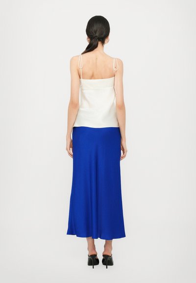 Camiseta de seda blanca con tirantes ajustables, combinada con una falda larga y fluida de color azul real. Texturas suaves en toda la ropa.