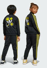 Black tracksuit with yellow stripes. Features a graphic with smiley faces on the back. Includes black pants and white/yellow sneakers.