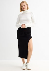Suéter de cuello alto blanco de punto y falda negra acanalada con una abertura alta en el muslo, combinados con zapatillas blancas. Diseño simple y ajustado.