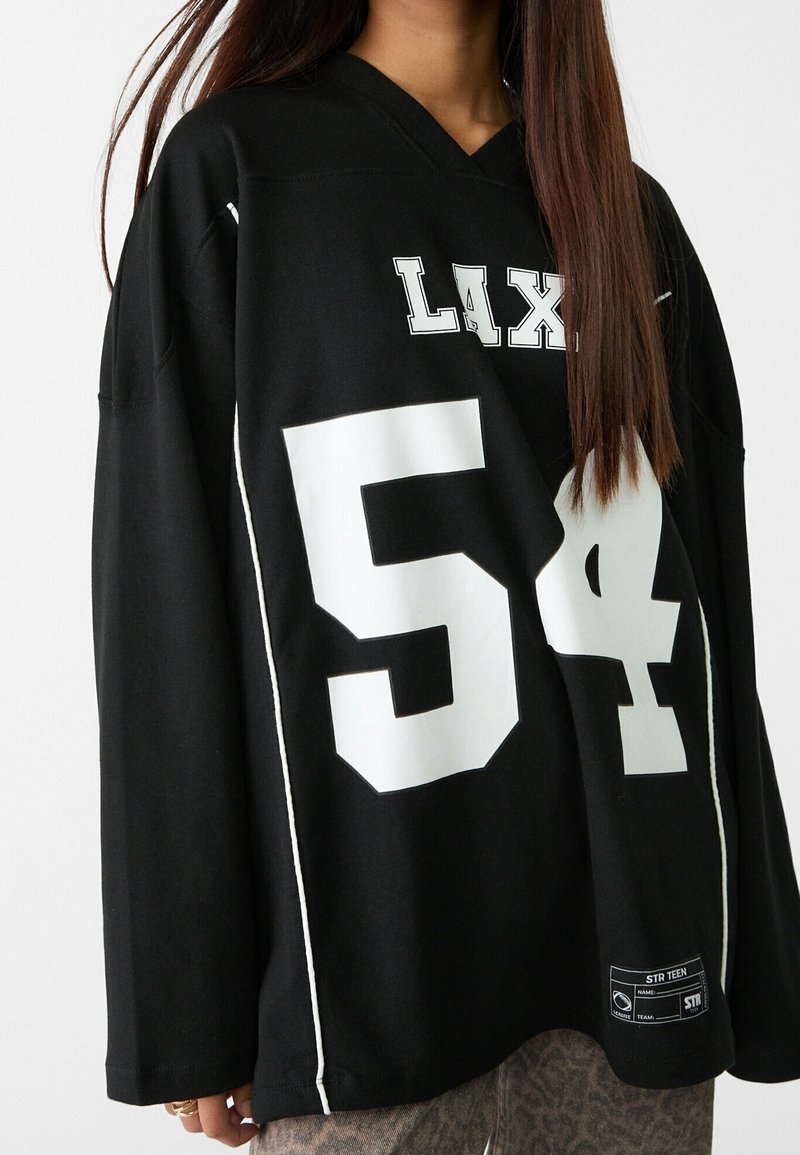 Maillot noir surdimensionné avec texte blanc "LAX" et le numéro "54" imprimés. Comprend un col en V, des manches longues et des détails de couture contrastés.