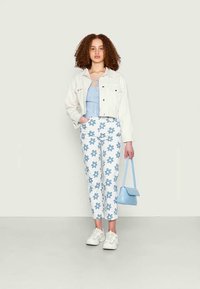 Top cropped azul claro, casaco de ganga branco, calças brancas com flores azuis e ténis brancos. A carregar uma pequena mala azul clara.