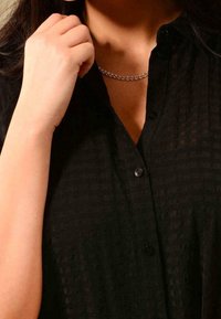 Černá strukturovaná košile s knoflíkovým zapínáním a límcem, s jemnými proužky. Stříbrný řetízek dodává detail.