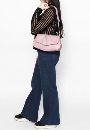 Borsa a tracolla in pelle rosa con forma arrotondata, caratterizzata da una cucitura ondulata e una tracolla. Indossata con un top nero a strisce trasparenti e jeans svasati.