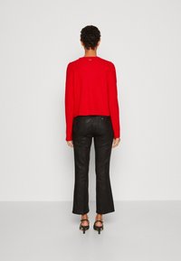 Pull court rouge en maille, associé à un pantalon noir évasé avec un motif texturé. Sandales à talons noires complètent la tenue.
