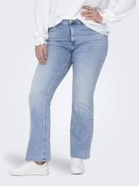Persoon draagt lichtblauwe jeans met rechte pijpen, witte casual sneakers en een witte blouse met lange mouwen en geplooide manchetten.