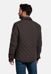 Gegoten jas in donkerbruin met een gladde textuur, met een kraag en een subtiele logo-detail op de mouw. Draag het over blauwe jeans.