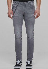 Szare, zniszczone dżinsy o dopasowanym kroju, z widocznymi przetarciami i łańcuszkiem na talii, w połączeniu z czarno-białymi sneakersami.