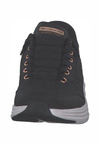 Schwarze Sportschuhe mit gesteppter Oberseite, roségoldenen Ösen und einer weißen Gummisohle. "SKECHERS COZY FIT" Branding auf der Zunge.
