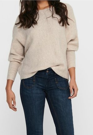 Maglione a maglia color beige chiaro con una vestibilità rilassata e polsini a coste, abbinato a jeans in denim blu scuro con cuciture sottili e cinque tasche.