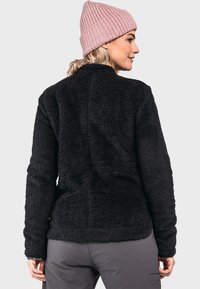 Schwarze Fleecejacke mit einer strukturierten Oberfläche, hohem Kragen und taillierten Ärmeln. Kombiniert mit einer hellrosa Strickmütze.