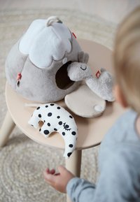 Kind reikt naar beige tafel met zacht grijs speelhuis en twee knuffels, een zwart-wit gevlekt en een grijze.