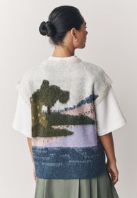 Gilet en maille duveteuse présentant un design paysager avec un arbre vert, des collines roses et de l'eau bleue, dans des couleurs pastel douces et une coupe décontractée.