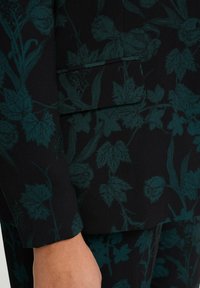 Svart tyg med teal blommönster; har blad och blommor; mjuk textur; skräddarsydd passform med synlig söm och fickdetalj.