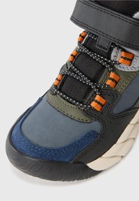 Calzature multicolore caratterizzate da un mix di materiali blu navy, verde, nero e arancione con superfici testurizzate, cinturini regolabili e lacci a fantasia.