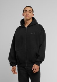 Black zip-up hoodie made of soft cotton material, featuring a front pocket and a drawstring hood, with a subtle white logo on the chest.