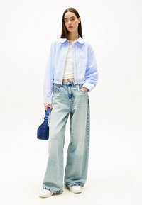 Giacca corta azzurra con colletto, canotta bianca e jeans azzurri a gamba larga e strappati. Presenta anche una borsa blu con una tracolla.