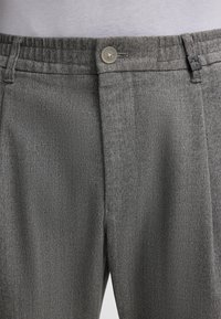 Gray woven trousers featuring a flat front design, elastic waistband, button closure, and minimal stitching details.
