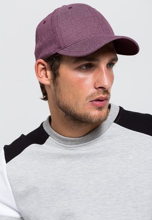 Bordeauxkleurige pet van gestructureerd materiaal met een gebogen rand, gedragen met een grijze sweatshirt met zwart-witte accenten.