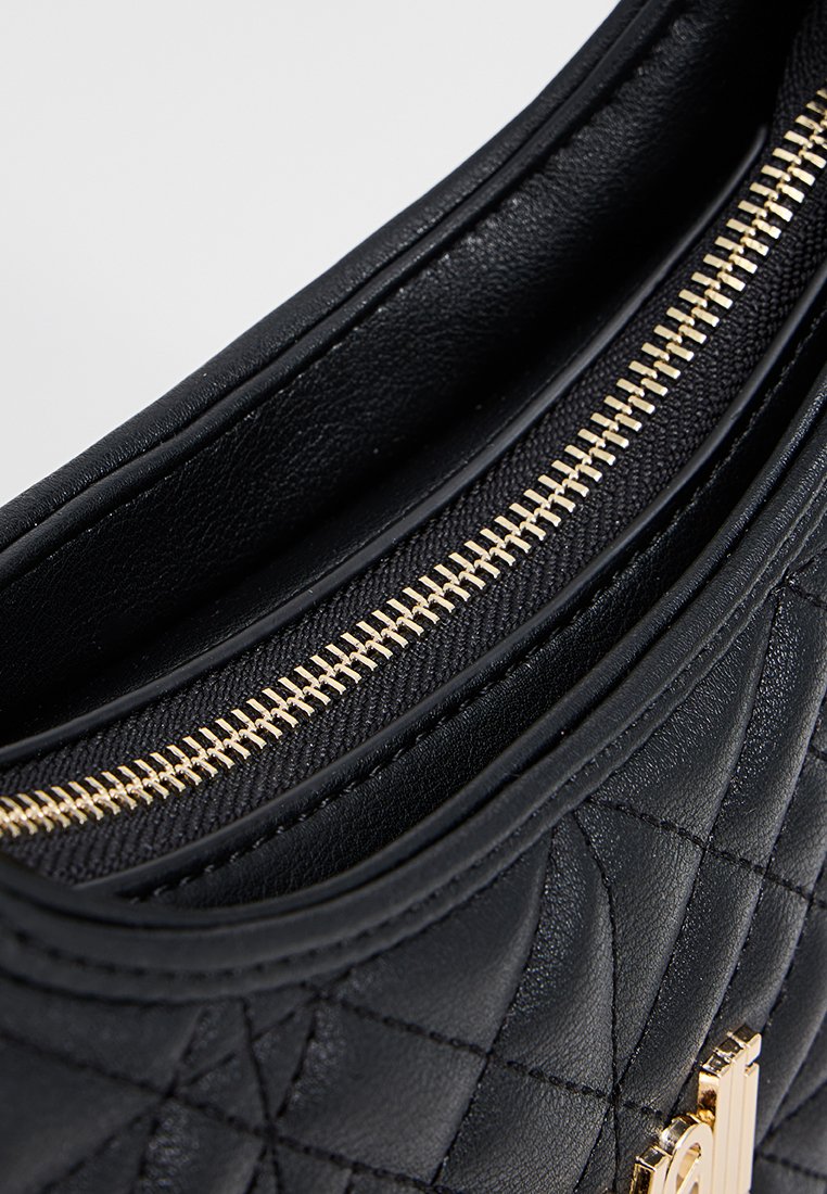 Schwarze gesteppte Lederhandtasche mit goldenem Reißverschluss, die eine glatte Textur und ein einfaches, modernes Design aufweist. Innenfutter sichtbar.