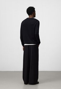 Felpa nera con scollo rotondo e maniche lunghe, abbinata a pantaloni neri larghi e svasati, con un orlo bianco a strati.