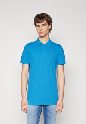 Camisa polo azul hecha de algodón, con cuello, mangas cortas y un pequeño logo de la marca en la parte izquierda del pecho.
