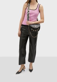 Růžový žebrovaný top bez rukávů s černými detaily, černé kožené kalhoty s vysokým pasem a černá taška přes rameno s zlatými akcenty a řetízkovým popruhem.