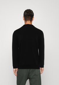 Felpa nera a maniche lunghe con collo a girocollo, texture liscia e vestibilità comoda, abbinata a pantaloni verdi. La vista posteriore non mostra loghi visibili.